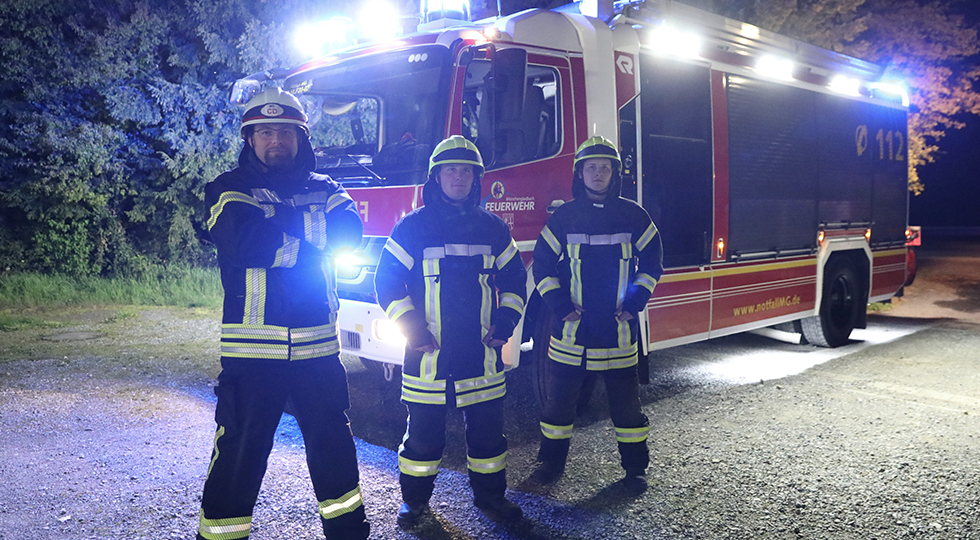 3 Mitarbeiter der Feuerwehr-MG vor einem Feuerwehrwagen